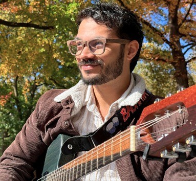 An IME instructor with a guitar under autumn trees